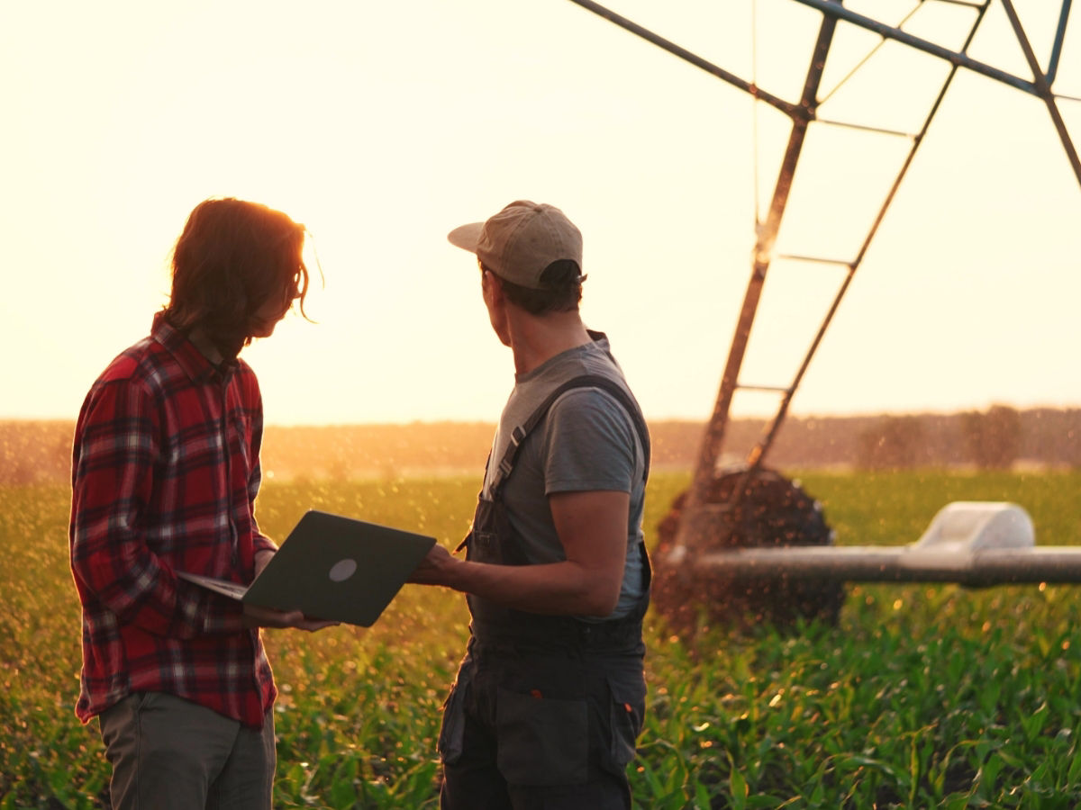 Zwei Männer mit Laptops, die eine landwirtschaftliche Fläche inspizieren