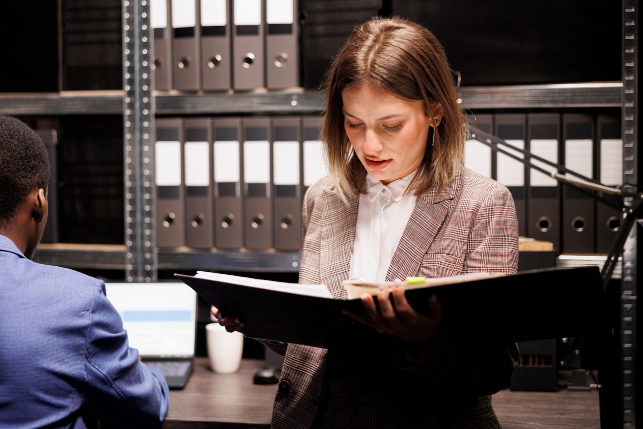 Professional reviews files in an office with organized shelves and binders, representing systems integration and information management work.