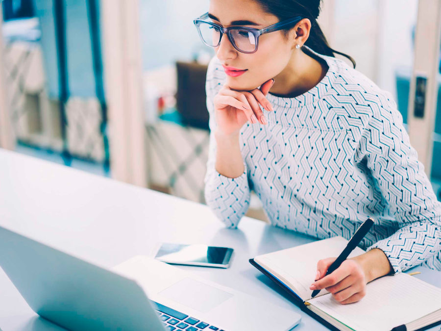 Woman on table taking notes in front of laptop