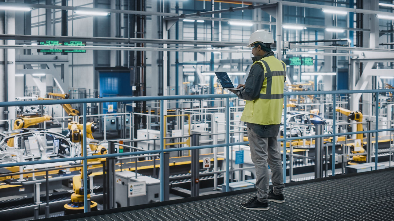 Techniker in einem Automobilwerk mit einer Sicherheitsweste bei der Arbeit am Notebook