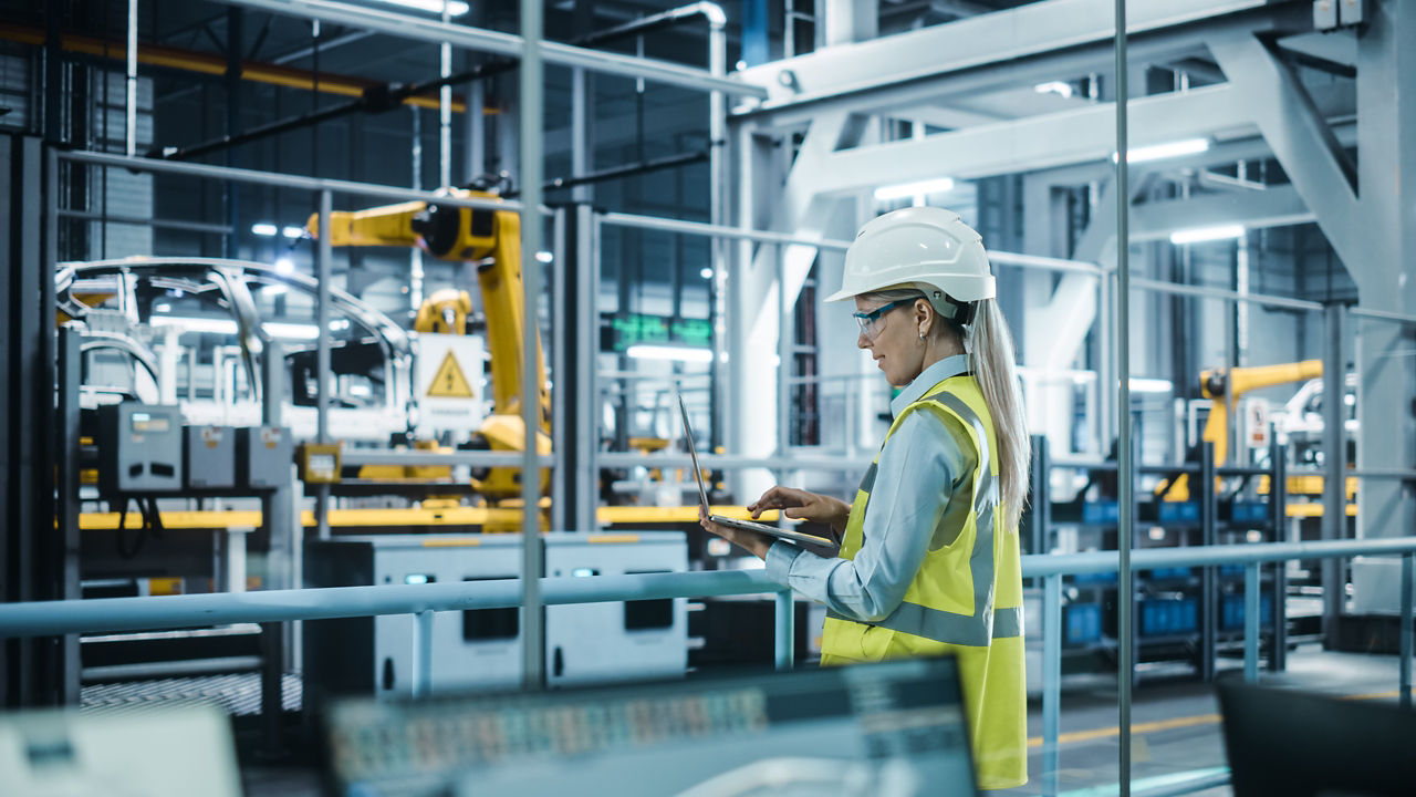 Female automotive engineer wearing hard hat using a laptop in a car factory