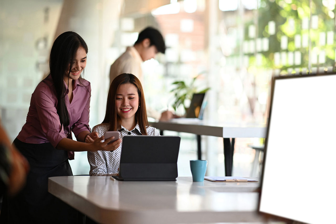 Dos jóvenes empresarias discuten su proyecto sobre una tableta digital y un teléfono inteligente en una mesa de reuniones.