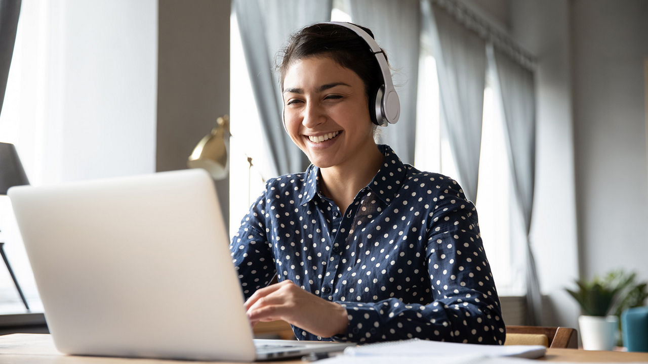 Mulher sorridente sentada à mesa, trabalhando no laptop e escrevendo em um caderno