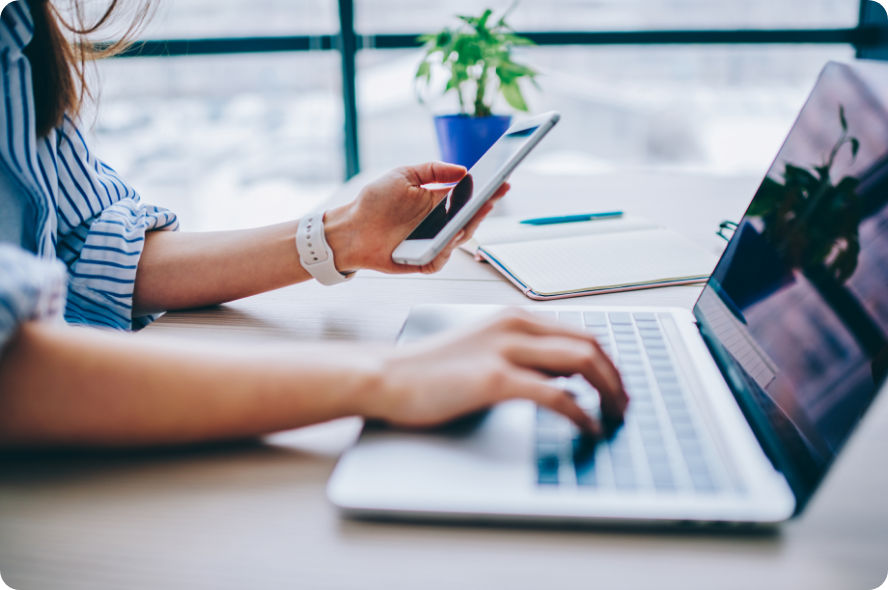 A woman using a laptop and smartphone at her office desk