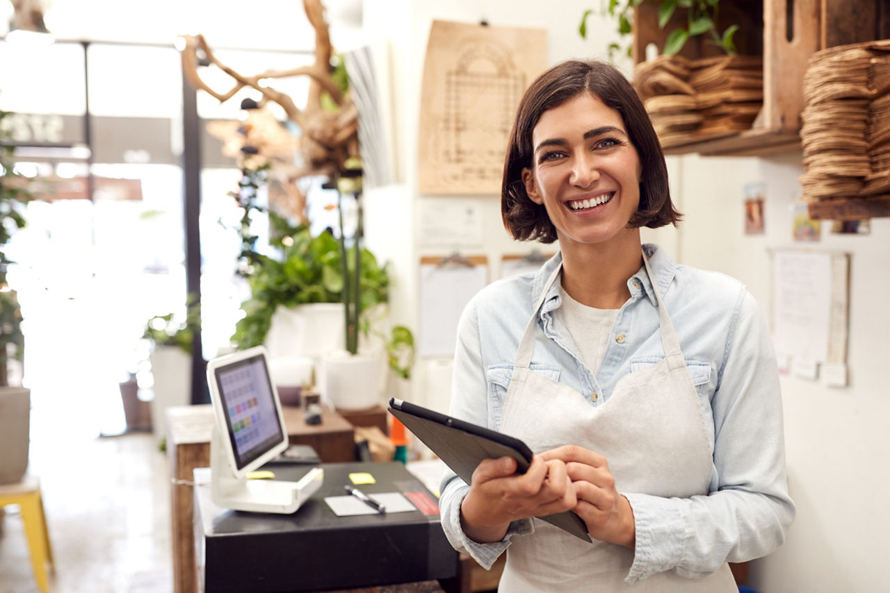 Portrait Of Female Owner With Digital Tablet Standing Behind Sales Desk Of Florists Store