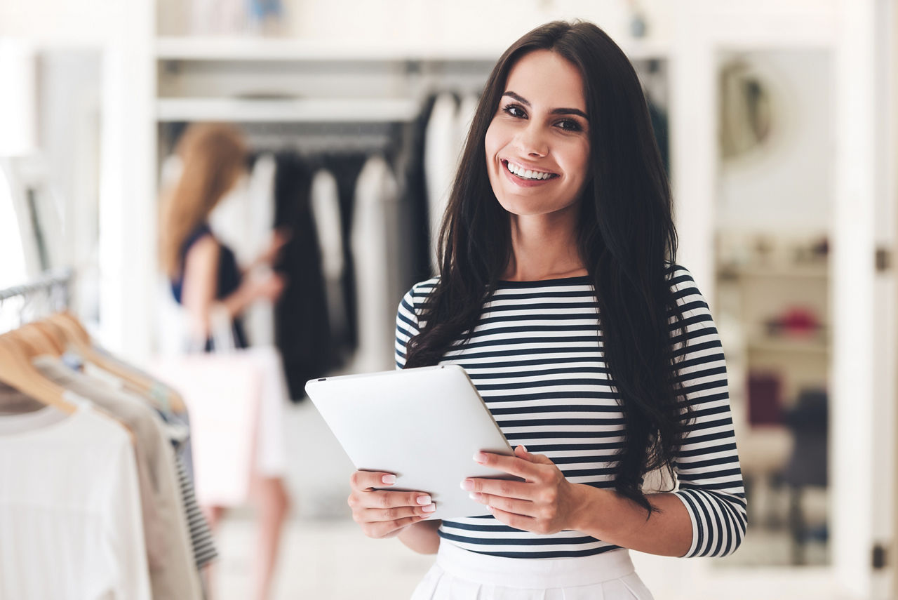 デジタル タブレットを抱えて働く洋服店の若い女性