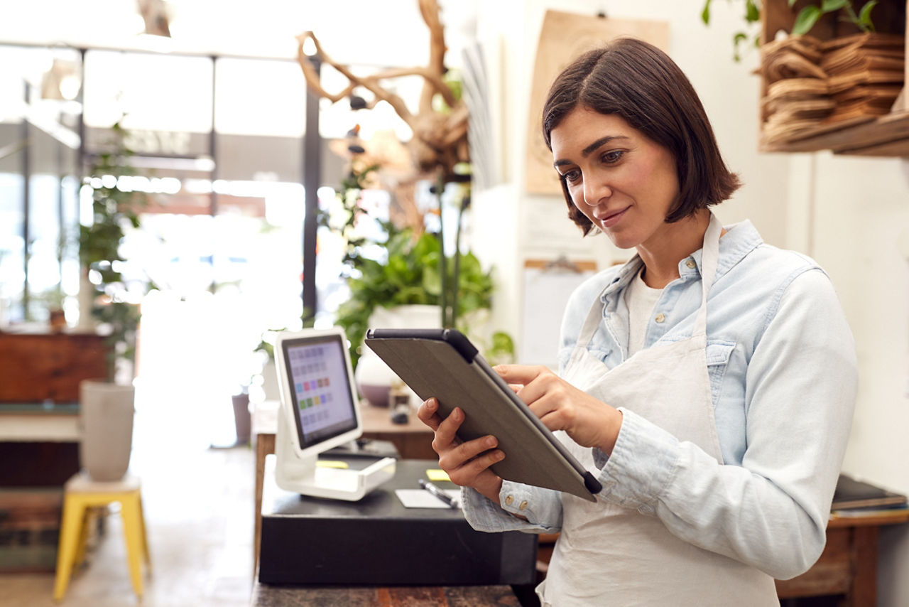 Proprietária com tablet digital em pé atrás de um balcão de vendas de uma floricultura