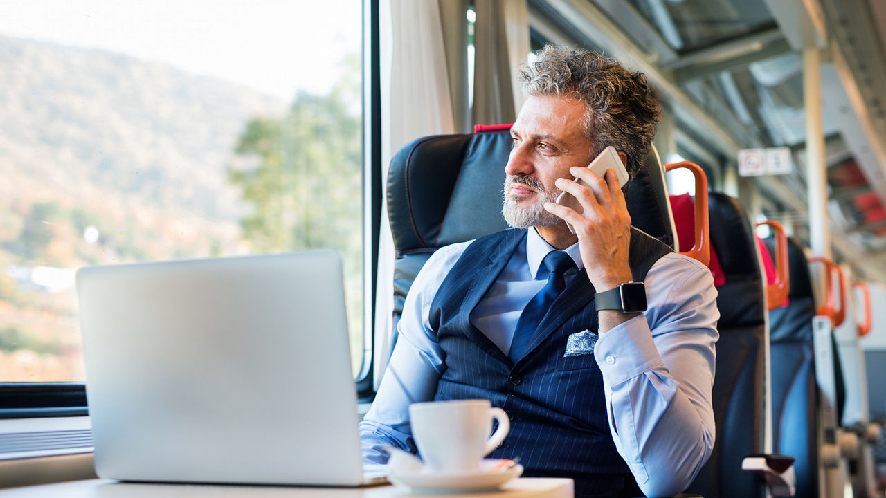 Homme assis dans un train, travaillant sur son ordinateur portable et répondant à un appel