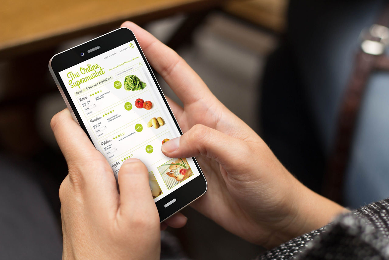 Garota usando um telefone digital com um supermercado online na tela