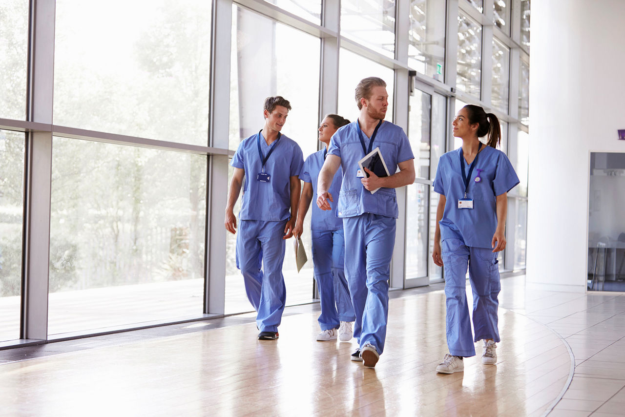 Quatro profissionais da saúde em uniformes caminhando no corredor