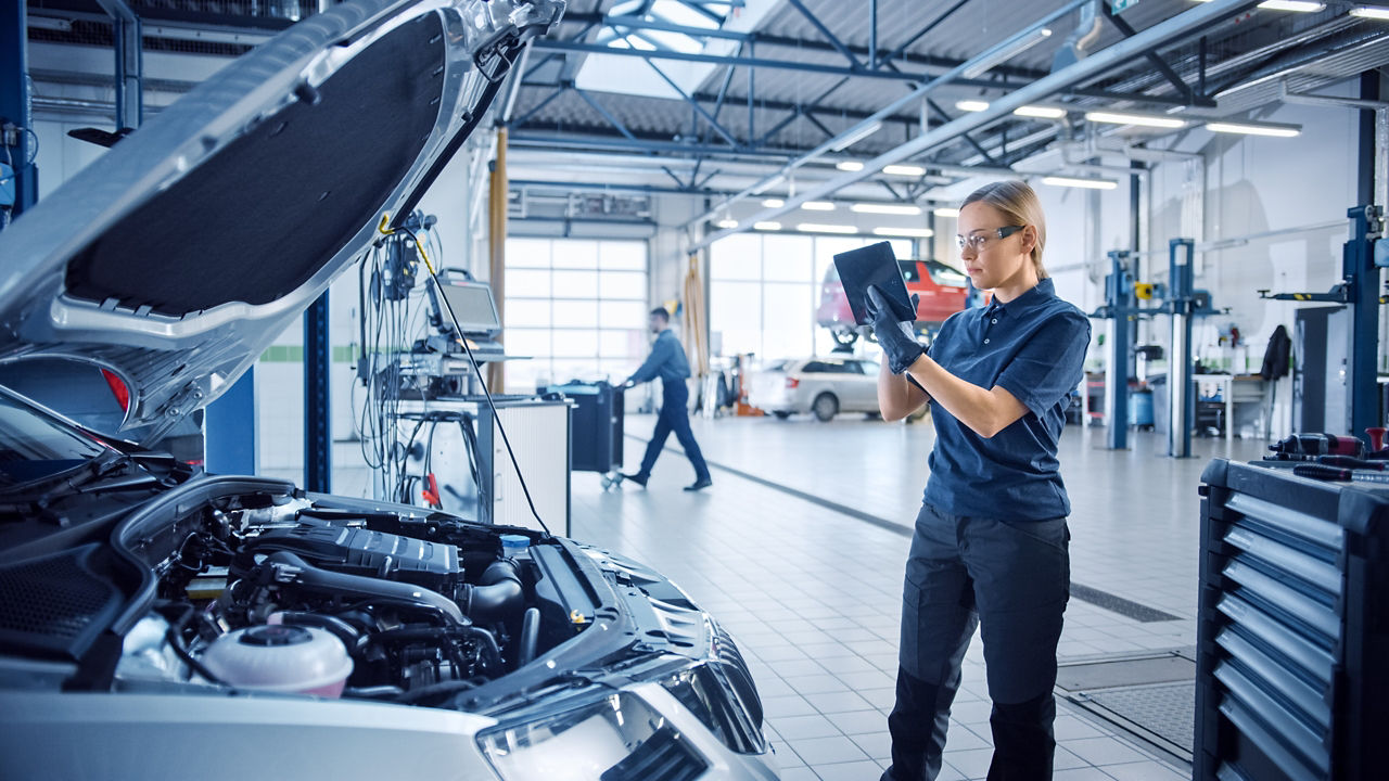 Mulher profissional de mecênica usando um tablet com um software de diagnóstico de realidade aumentada em um ambiente moderno de serviço automotivo